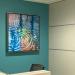 On the wall above a reception desk hangs a painting of ripples in water. the colors are blue with some green and orange. 