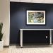 a framed artwork hangs above a table on a black wall