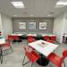 three framed artworks hanging on wall behind room of tables with red chairs